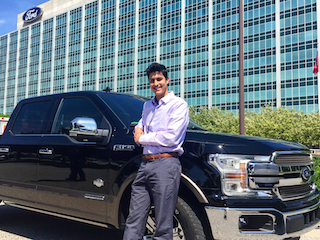 A man leaning on a black F-150 outside a glass headquarters building