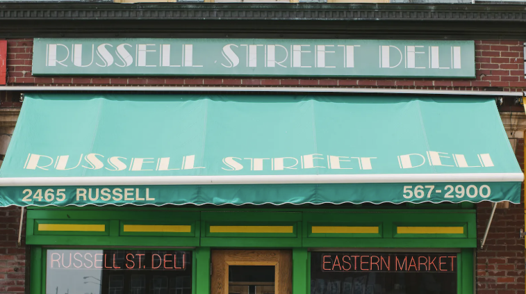 A deli's green awning and neon signs on a market street